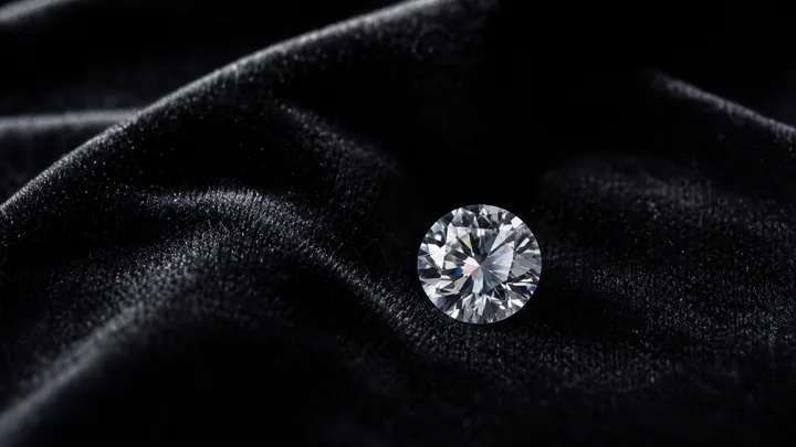 A round brilliant natural diamond rests on black velvet under directional jewellery studio light.